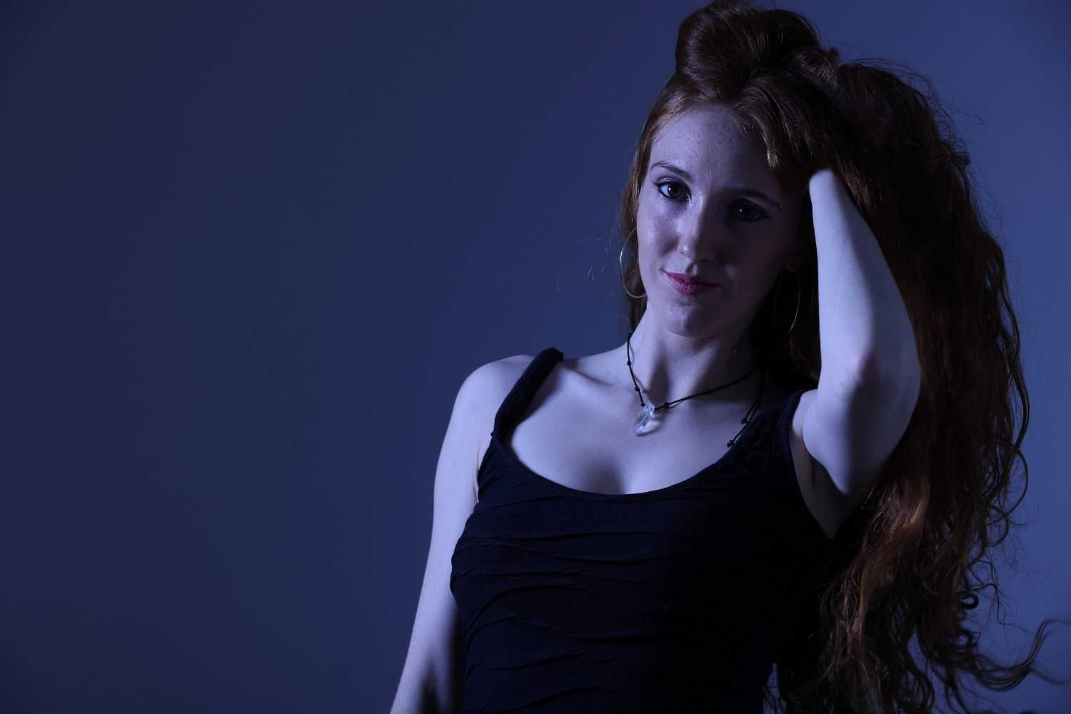 Woman with red hair posing in blue lighting.